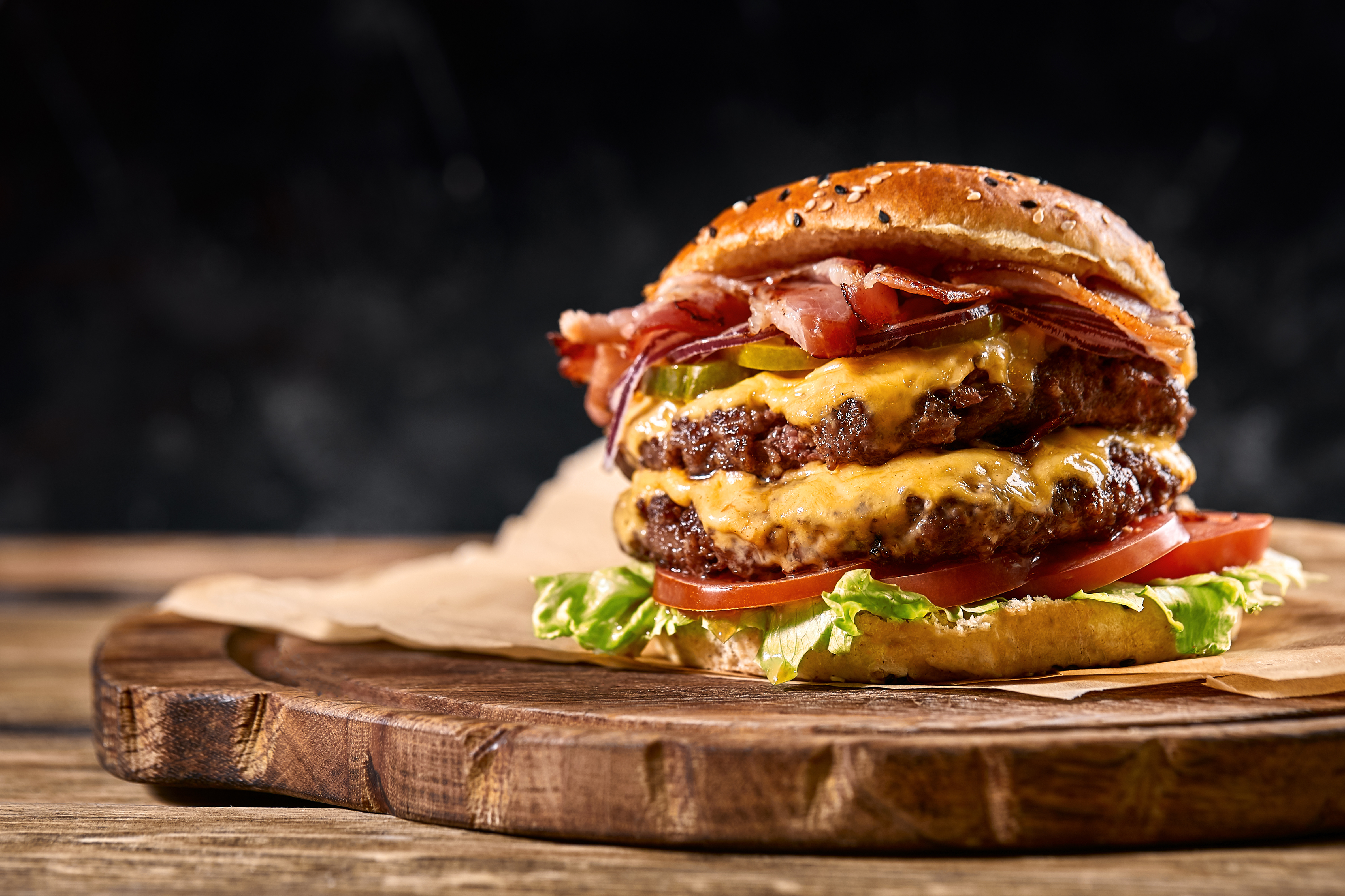 Juicy American burger, hamburger or cheeseburger with two beef patties, with sauce and basked on a black background. Concept of American fast food.