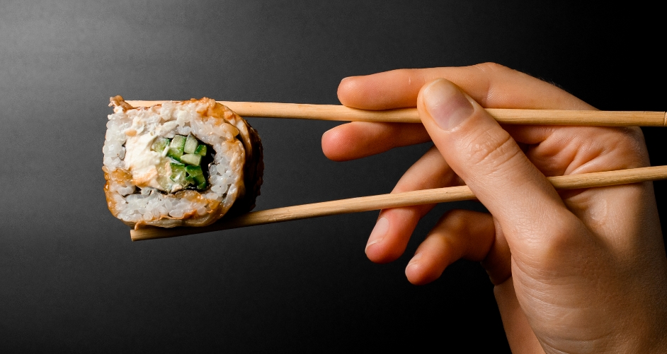 Sushi being held by chopsticks on black background